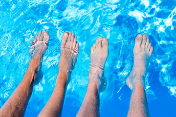 Four bare legs feet in water of swimming pool