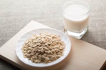 Saucer with dry cereal on a wooden board and a glass of milk