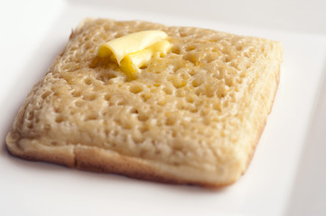 Buttered wheat crumpet on plate