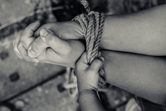 Thick rope ties the hands of women. Child's hand holding a rope.
