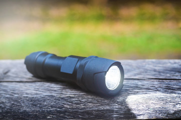 Tactical waterproof flashlight on wooden base with light beam