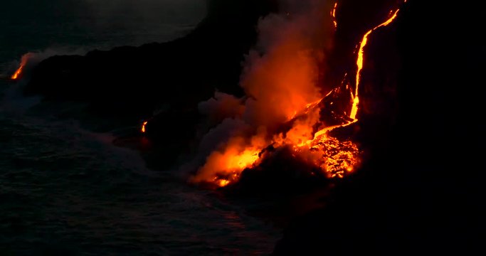 Hawaiian Lava flow from Kilauea volcano Hawaii at night. Steam rising from waves as molten lava flows into ocean waters Big Island Hawaii