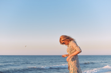 Beautiful adult attractive joyful blonde woman in dress on outdoors background blue sky