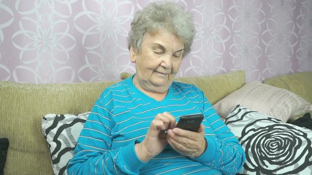 Old lady using a mobile phone sits on a beige sofa