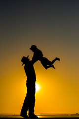 Fototapeta na wymiar Joyful silhouette of father throwing up his child at sunset outdoors background