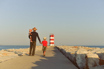 Back view of male with kids walking to the red lighthouse, sunny outdoors background