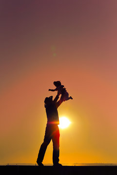 Joyful silhouette of father throwing up his child at sunset outdoors background
