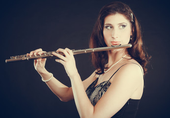 Woman playing transverse flute on black.