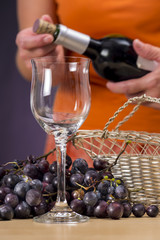 Woman opening a bottle of red wine, behind a glass stemware and cluster of red grapes