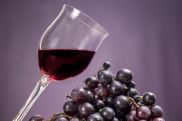 Cup of red wine beside red grapes, on purple background