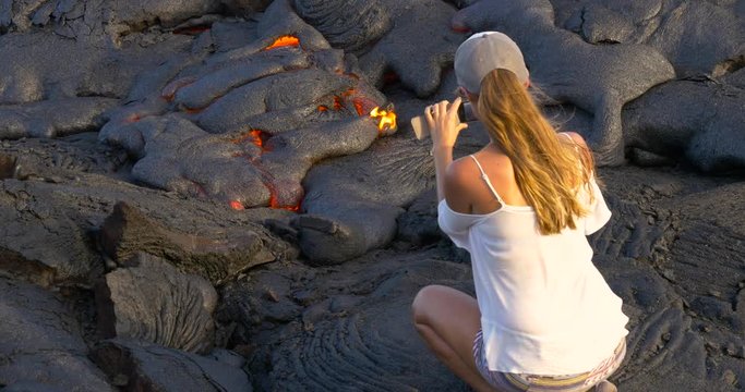 Girl taking picture flowing lava in Kilauea volcano Hawaii.Tourist taking photo of flowing lava from Kilauea volcano around Hawaii volcanoes national park, USA.