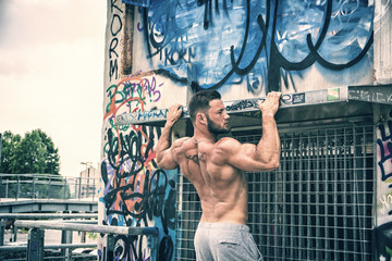 Portrait of tattooed topless sportsman doing abs exercise on metal railing outdoor