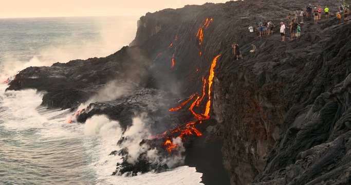Tourist looking at Volcanic Eruption Lava flowing into the ocean. Steam rising from waves as molten lava flows into ocean waters Big Island Hawaii.