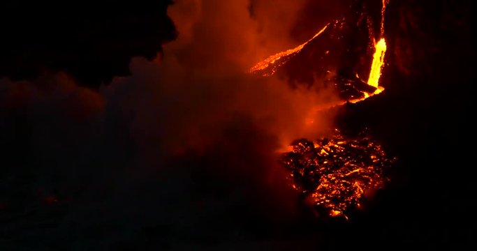 Volcanic Eruption Lava flowing into the water Hawaii at night. 
Steam rising from waves as molten lava flows into ocean waters Big Island Hawaii.