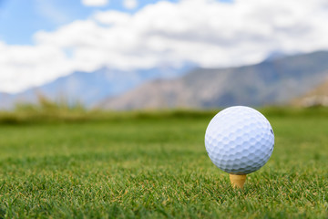 Closeup of golf ball on a tee, on golf course with mountains in the background
