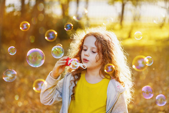 A little girl blowing soap bubbles in autumn park. Background to