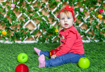 Little girl sitting in the park on the grass in a sunny summer day and playing with apples.