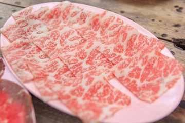 Pieces of raw fresh paper-thin sliced beef for grill to make Japanese yakiniku on plate.