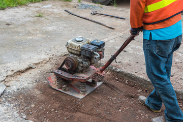 Worker reversible plate compactor on a roadwork site. Excavator in background.Repair cracked Sidewalk