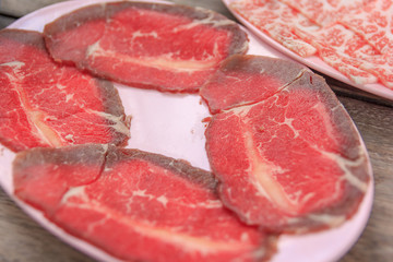 Pieces of raw fresh paper-thin sliced beef for grill to make Japanese yakiniku on plate.