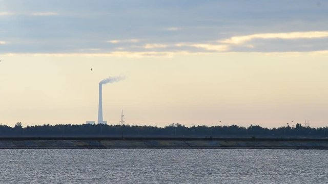 Smoke stack. Smoke coming out of industrial chimney far off with water in foreground and colorful sky