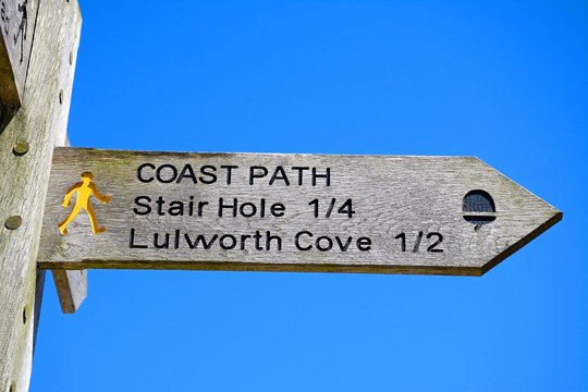 Wooden Lulworth Cove signpost against a blue sky.