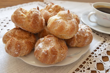 Delicious, small homemade cream puffs powdered with icing sugar on white plate and cup of coffee
