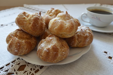 Delicious, small homemade cream puffs powdered with icing sugar on white plate and cup of coffee
