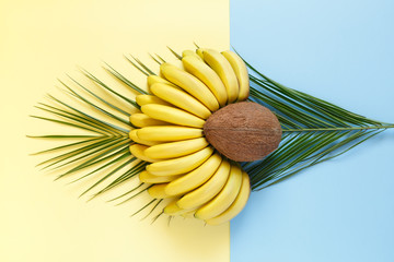 Coconut and bananas on palm leaves on a bright color background.