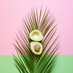 Fototapeta premium Dojrzały Avocado na palmowym liściu na barwionym tle. Minimalna koncepcja