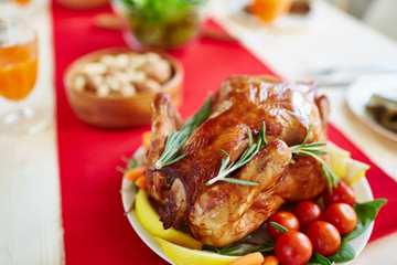Closeup of delicious glistening roasted turkey on plate of vegetables, decorated with lemon and rosemary, waiting for guests on festive dinner table