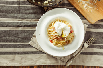 Overhead view of plate of spaghetti Carbonara with poached egg. Rustic styled