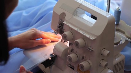 Woman treated tissue using overlock. Cuts the fabric edge. Women's hands. Quickly sew close-up.