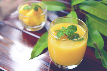Ripe yellow mango juice, mint leaf on top with fruit and leaf on wooden background.