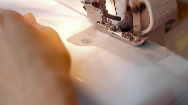 Woman treated tissue using overlock. Overlock foot closeup. Women's hands. Sewing machine.