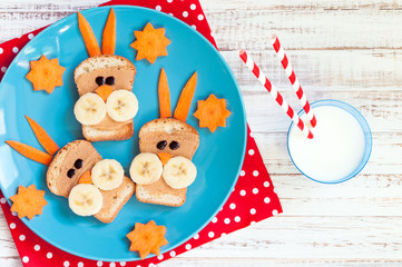 Children's breakfast with sandwiches and milk. Funny rabbit face sandwiches with peanut butter, banana and carrots