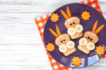 Children's breakfast - funny rabbit face sandwiches with peanut butter, banana and carrots. Top view