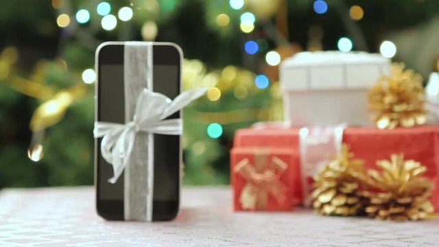 Smartphone with Christmas gifts and decorations in front of Christmas tree.