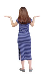 back view of woman protects hands from what is falling from above. brunette in a blue striped dress raised her hands, palms up.