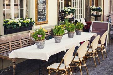 Fototapeta na wymiar Сozy outdoor cafe in Europe with white tablecloth and flower ba