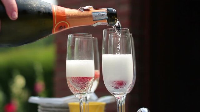 Close up shot of someone pouring champagne to glasses in the summer outdoors, slow motion