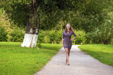 Young beautiful woman in brown dress walks in the summer park