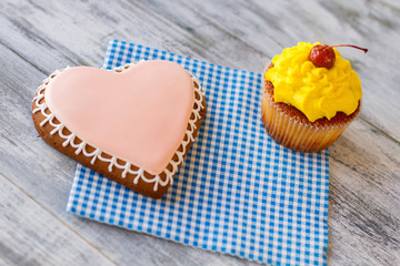 Heart cookie and yellow cupcake. Pastry on blue napkin. Make present for beloved one. Sign of attention and care.