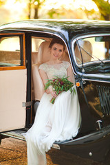Lovely and happy bride is sitting in black retro car