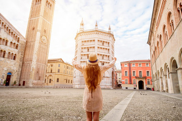 Young female tourist standing back on the central square with cathedral and famous leaning tower on the background in Parma town. Having great vacations in Parma
