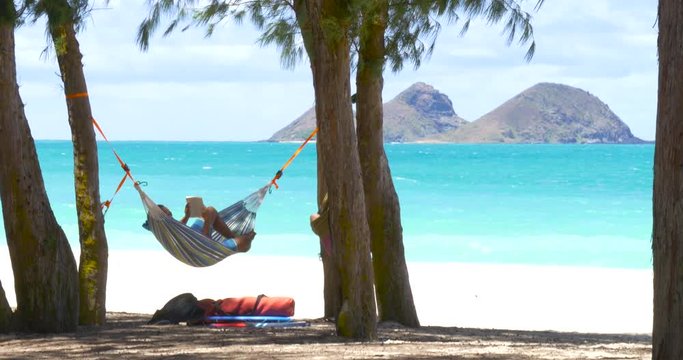 Young man reading a book on hammock exotic beach in Hawaii Oahu.