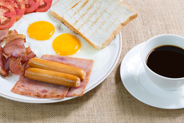 American breakfast, bacon, fried egg, ham and sausage in white d