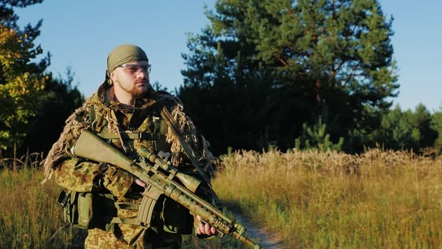A man in a camouflage bandanna and walking along a country road. In the hands holding weapons
