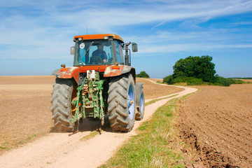 Obraz premium Tractor driving on Dirt Road through Ploughed Fields in Autumn Landscape
