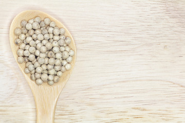 White pepper in wooden spoon on nature wood background for design.